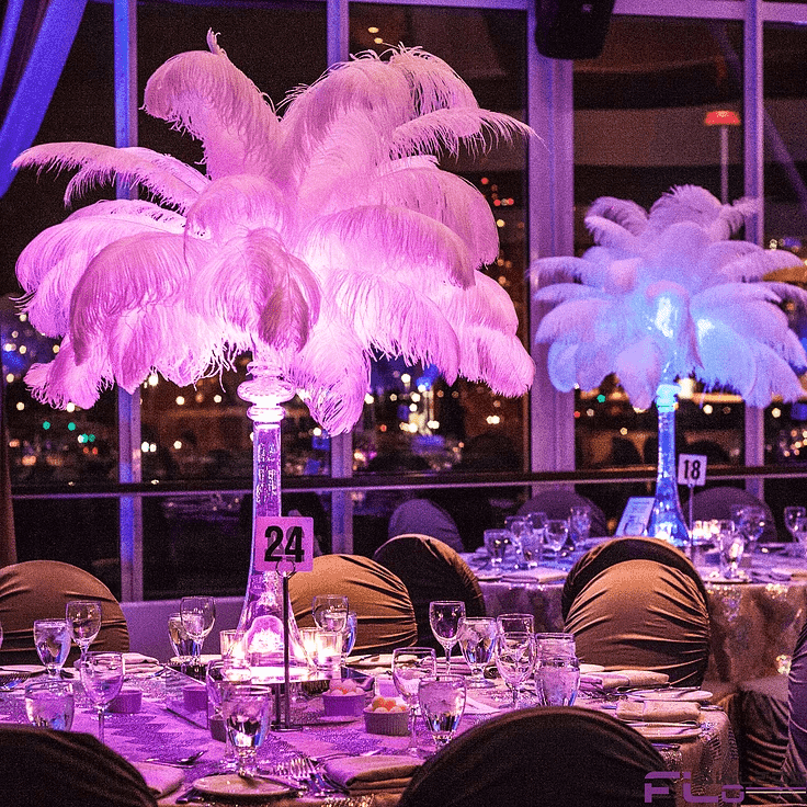 Tall feather centrepieces lit pink and blue on tables by the windows