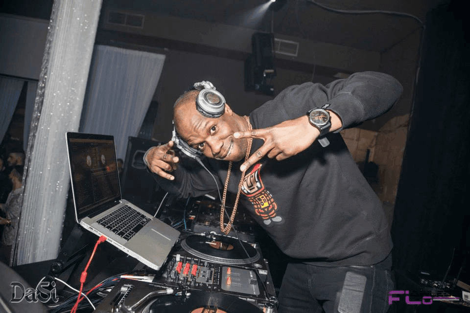 DJ in headphones posing at turntables and a laptop in the club booth