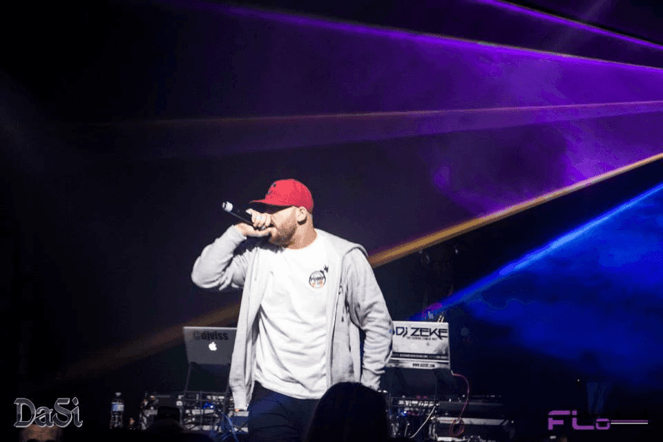 Rapper on mic in front of the DJ Zeke booth as purple and gold laser beams cross above