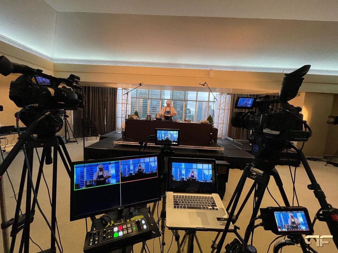Cameras and switcher framing a chef on stage against a skyline window