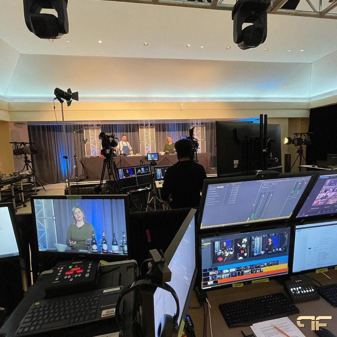 Livestream control desk facing a chef and host on a lit cooking stage