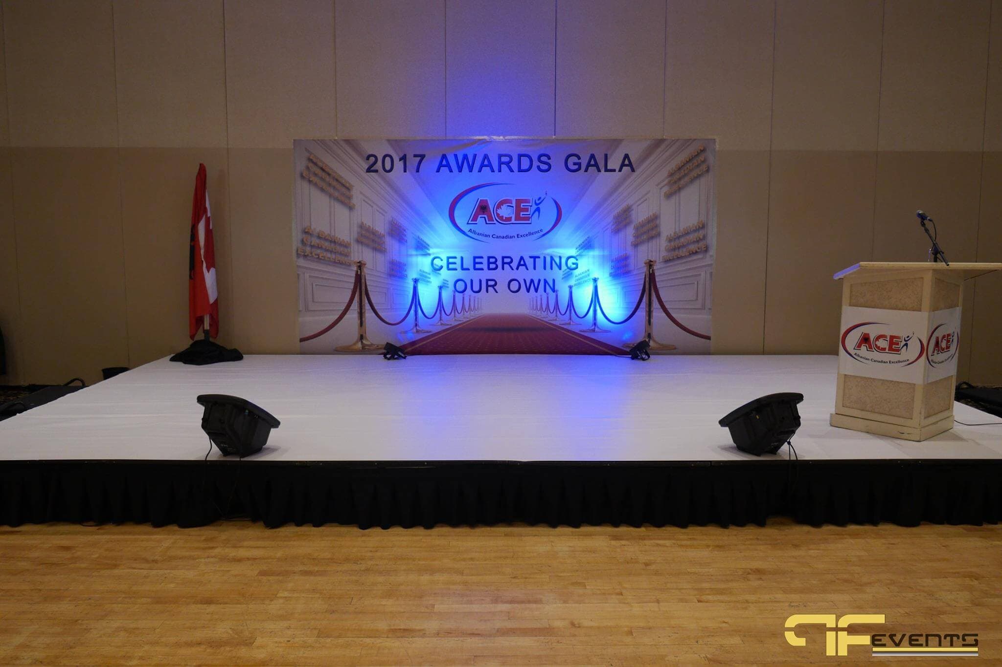 Stage with blue-lit ACE backdrop, floor monitors and Canadian flag