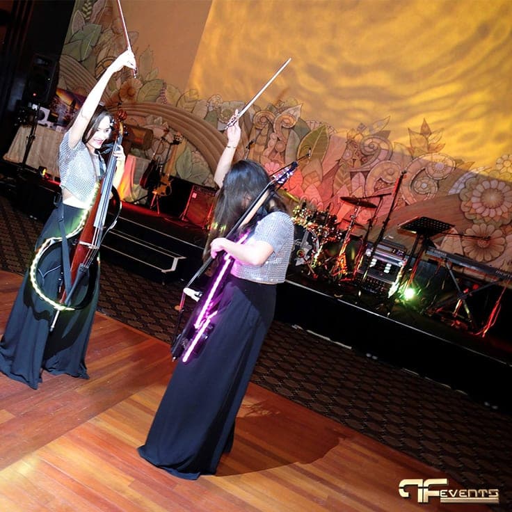Cellists raise their bows beside the band backline, gold light texture behind