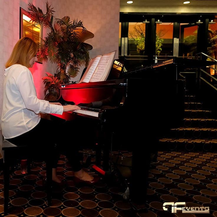 Pianist at a grand piano in the Eglinton Grand lobby under red uplighting