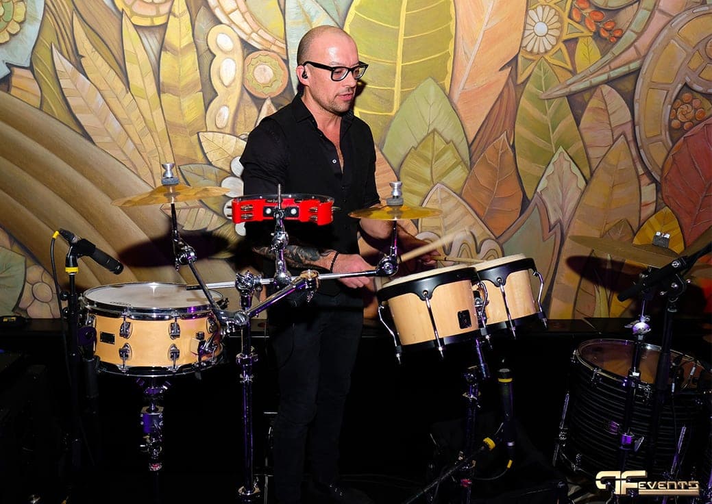 Percussionist with bongos, snare and tambourine, all miked, before the mural