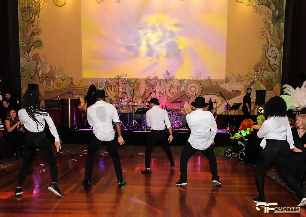 Dance crew in white shirts and black hats performing on the wood dance floor