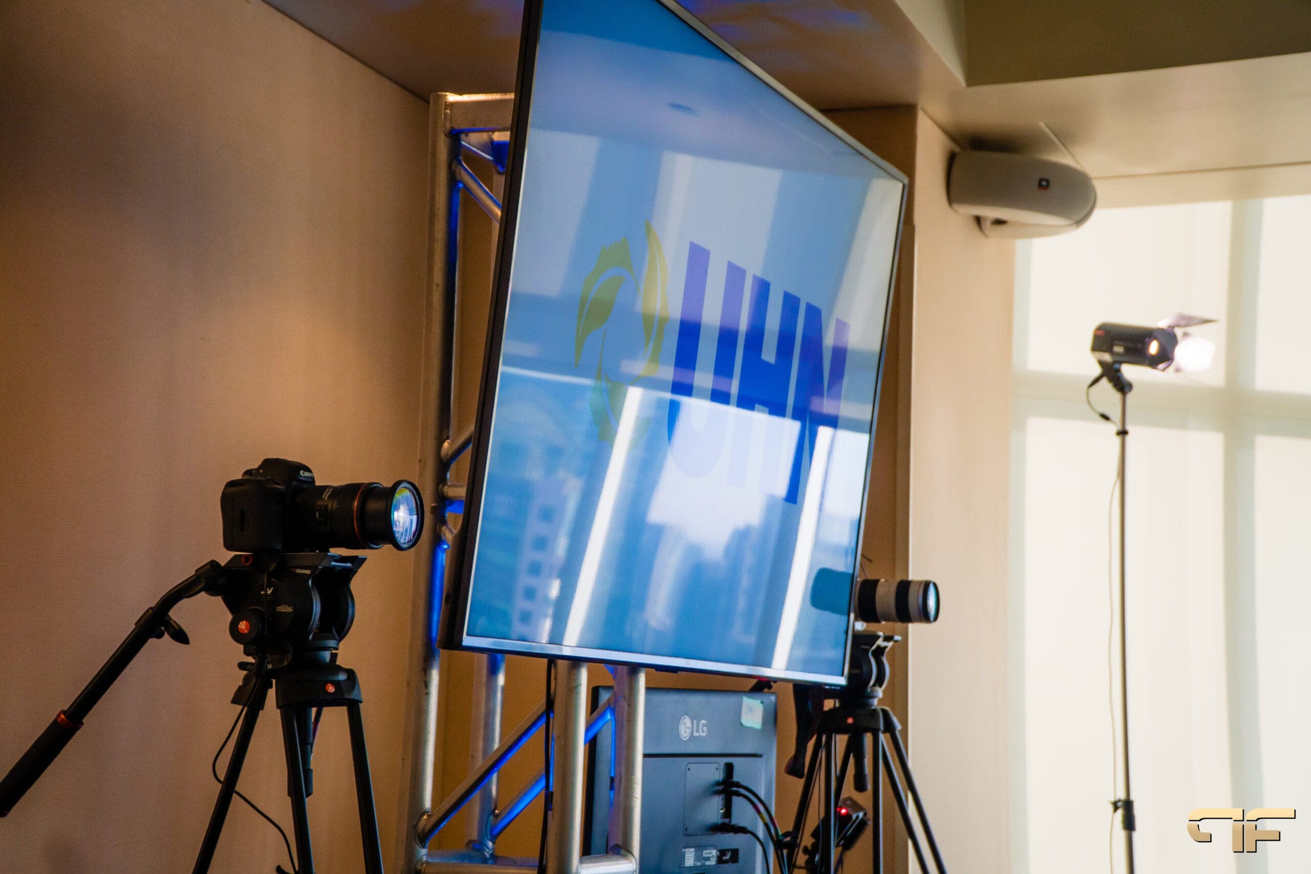 Cameras on tripods either side of a UHN screen, softlight by the window