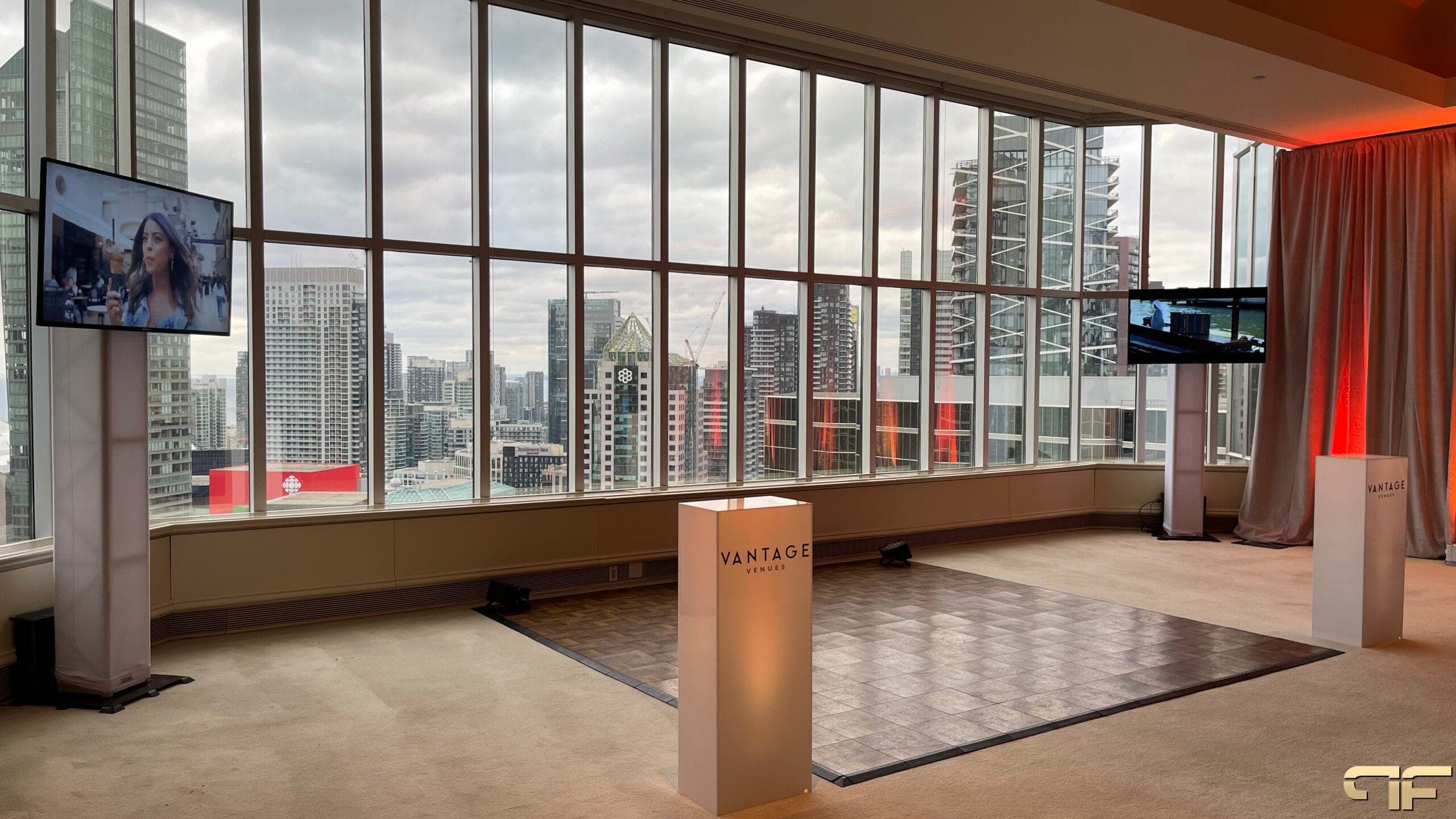 High-floor room with city-view windows, TVs on white totems, parquet floor, Vantage plinths