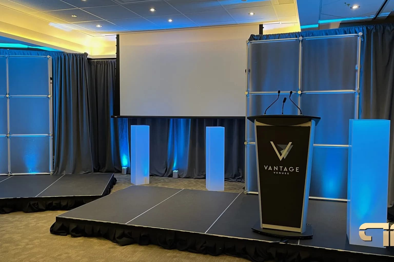 Corporate general session stage with a projection screen, a lectern, and blue uplighting, set before the audience arrives